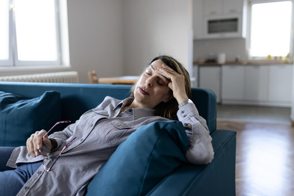 Person lying on a couch resting head on hand, appears fatigued or unwell, with a stressed expression