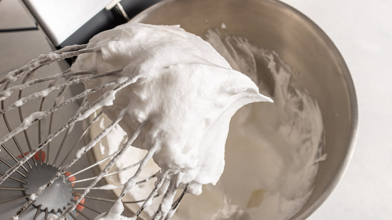 Balloon whisk with a stiff pick meringue on it over a stand mixer