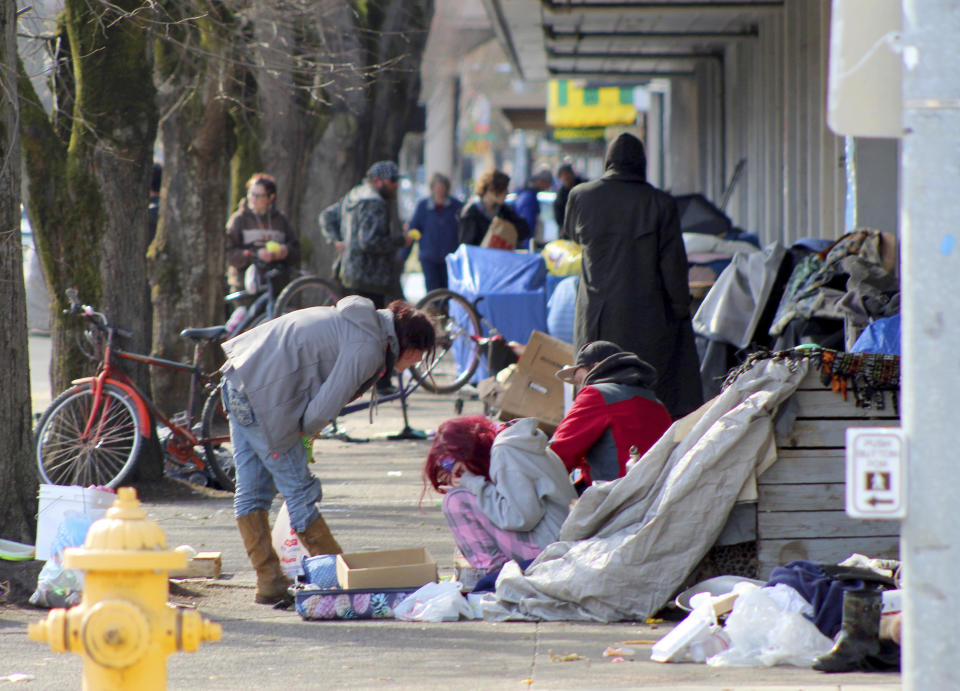 In this Tuesday, March 3, 2020 photo, homeless people crowd a sidewalk in downtown Salem, Ore., where they have set up a makeshift camp. Experts say that the homeless, who often have health and substance-abuse problems, are exposed to the elements and do not have easy access to hygiene, are more vulnerable to the coronavirus. Some cities are making provisions so the homeless who contract the virus have a place to recover without spreading the infection further. (AP Photo/Andrew Selsky)