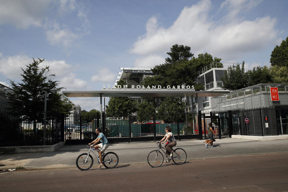 Parisinos pasean en bicicleta frente a la entrada del complejo de Roland Garros, sede del Abierto de Francia de tenis, el domingo 24 de mayo de 2020. (AP Foto/Francois Mori)