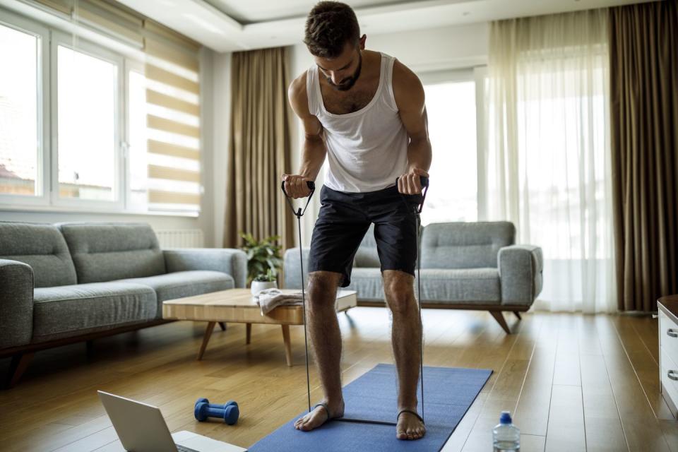 young athletic man training with resistance bands at home