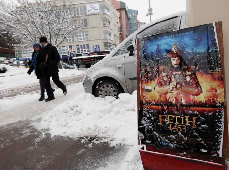 People walk past an advertisement for "Conquest 1453" displayed in snow outside a cinema in Ankara, Turkey, Wednesday, Feb. 29, 2012. Turkey is on a roll these days, uplifted by economic growth and regional diplomacy. Now comes a film to boost the feel-good mood, an epic about the 15th century fall of Constantinople that fuses Turkish nationalism with Hollywood-style ambition. "Fetih 1453," or "Conquest 1453," casts good guys (read Muslim Ottomans) against bad guys (aka Christian Byzantines), transforming a clash of empires and religions into a duel between right and wrong. (AP Photo/Burhan Ozbilici)