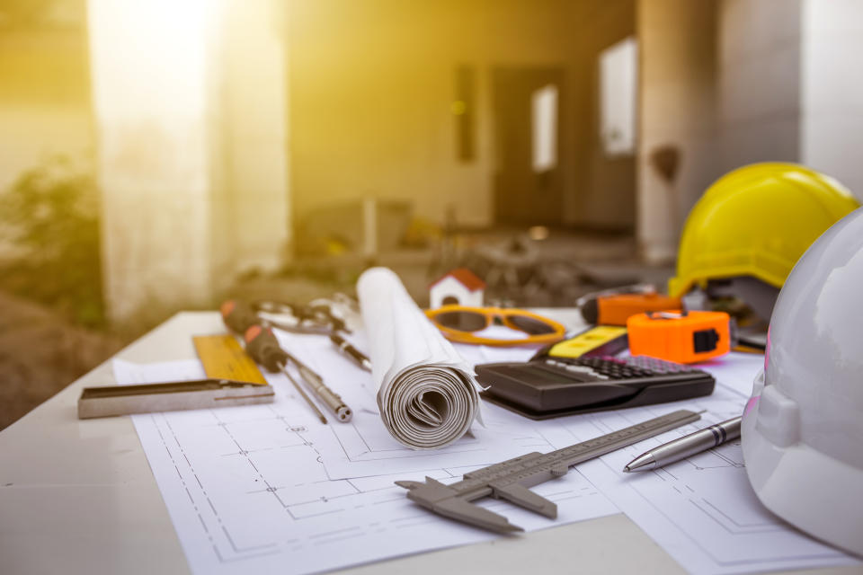 Drafting plans on a table with some tools and a hard hat