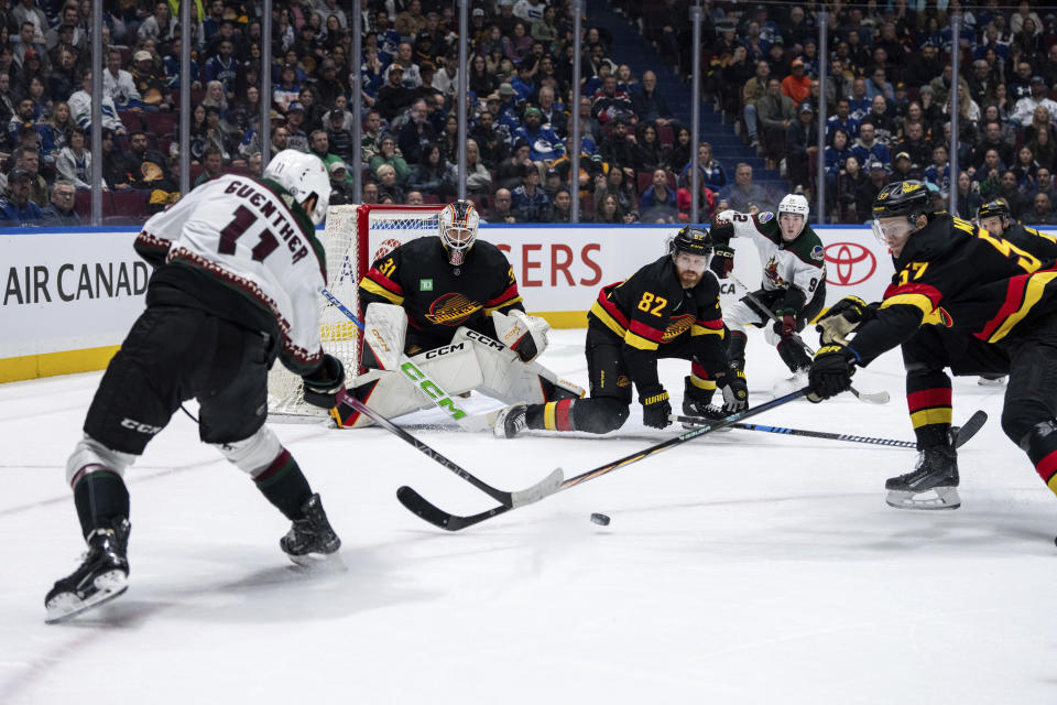 Arizona Coyotes' Dylan Guenther (11) passes the puck to Logan Cooley (92), who scored on Vancouver Canucks goaltender Arturs Silovs (31) as Ian Cole (82), and Tyler Myers (57) defend during overtime in an NHL hockey game Wednesday, April 10, 2024, in Vancouver, British Columbia. (Ethan Cairns/The Canadian Press via AP)