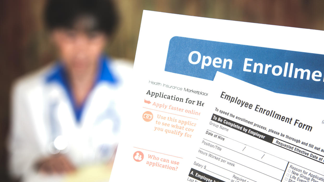 Patient holding open enrollment healthcare benefits forms with a medical doctor in the background.