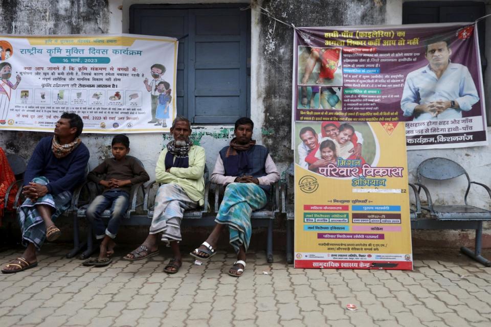 Men sit next to a board in Belwa village displaying information about the different family planning methods available (Reuters)