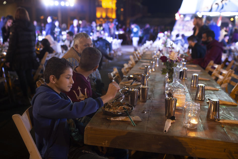 In this Monday, Dec. 23, 2019 photo, a boy eats with his brother and father at a public Christmas dinner in Martyrs Square where anti-government activists are encamped in Beirut, Lebanon. As an entrenched political class fails to chart a way out of Lebanon's economic crisis, despite weeks of street protests, some Lebanese resort to what they’ve done in previous crises: They rely on each other. (AP Photo/Maya Alleruzzo)