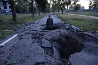 FILE - Viktor Shevchenko stands in a crater to show its depth after a Russian attack in the Saltivka district in Kharkiv, Ukraine, July 1, 2022. As Russia's invasion of Ukraine grinds into its fifth month, some residents close to the front lines remain in shattered and nearly abandoned neighborhoods. One such place is Kharkiv's neighborhood of Saltivka, once home to about half a million people. Only perhaps dozens live there now, in apartment blocks with no running water and little electricity. (AP Photo/Evgeniy Maloletka, File)