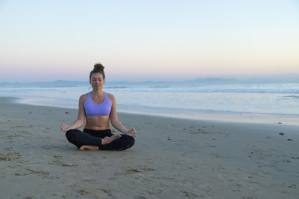 Woman meditating on the beach in the evening