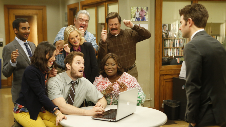 The cast of Parks and Rec looks at a laptop, while Ben who looks at the group