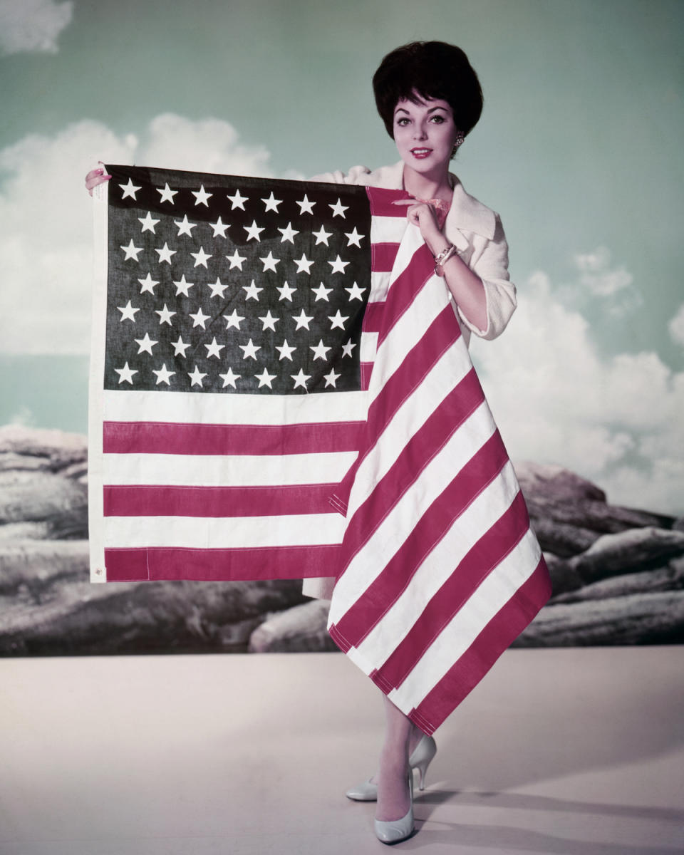 Joan Collins, British actress, holding the Stars-and-Stripes flag of the United States in a studio portrait, circa 1955 vintage 4th of July