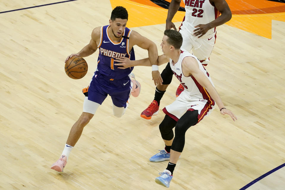 Phoenix Suns guard Devin Booker (1) drives as Miami Heat forward Precious Achiuwa, right, defends during the first half of an NBA basketball game, Tuesday, April 13, 2021, in Phoenix. (AP Photo/Matt York)