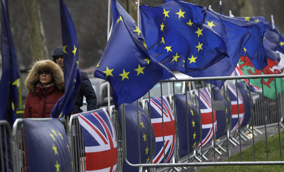 People dressed for the cold weather pass by flags tied to railings outside parliament in London, Thursday, Jan. 24, 2019. The European Union's chief Brexit negotiator, Michel Barnier, is rejecting the possibility of putting a time limit on the "backstop" option for the Irish border, saying it would defeat the purpose. (AP Photo/Kirsty Wigglesworth)