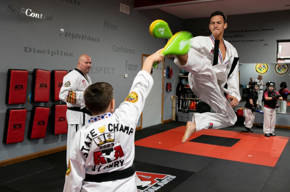 Fifth degree Black Belt and instructor owner Michael Poole (middle in background) watches as Liam Kinder, 16 of Carroll, practices his kicks as Jaxon Lowry, 10 of Lancaster, holds a target for him to kick inside of the Lancaster ATA Martial Arts on July 31, 2023, in Lancaster, Ohio. The Taekwondo students, along with instructor Michael Poole, went to the ATA World Championships in Phoenix, Arizona where Kinder took third in traditional sparring, and Evelyn Hill (not shown), 16, took first place in extreme weapons. Lowry did not place in worlds but won first place in traditional sparring and combat at the state level championship.