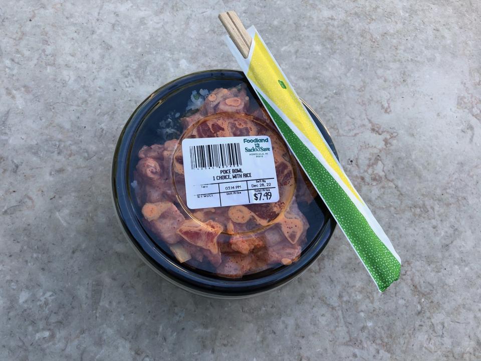 A spicy ahi poke bowl with white rice and furikake from Sack N Shave on a stone table with a pair of disposable chopsticks resting on top.