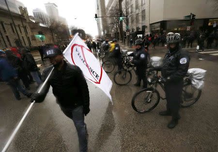 A demonstator carrys a flag under the watchful eye of Chicago Police Department officers as they gather to protest last year's shooting death of black teenager Laquan McDonald by a white policeman and the city's handling of the case at an intersection in the downtown shopping district of Chicago, Illinois, November 27, 2015. REUTERS/Jim Young