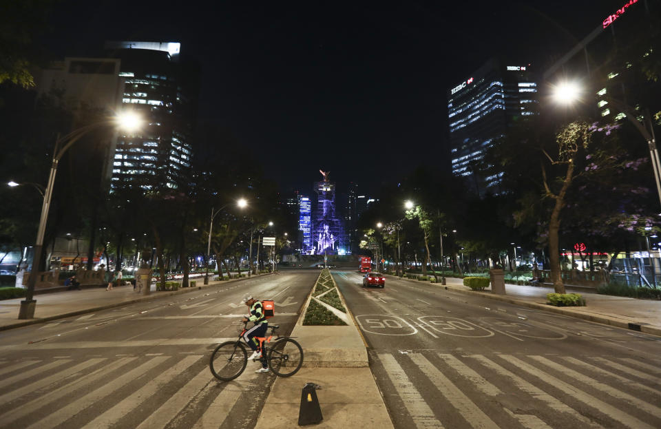 A food delivery worker crosses Reforma Avenue, normally congested with traffic, in Mexico City, Friday, March 27, 2020. City authorities announced measures to deal with the new coronavirus such as closing bars, discos, museums, zoos, cinemas, theaters and gyms. (AP Photo/Eduardo Verdugo)