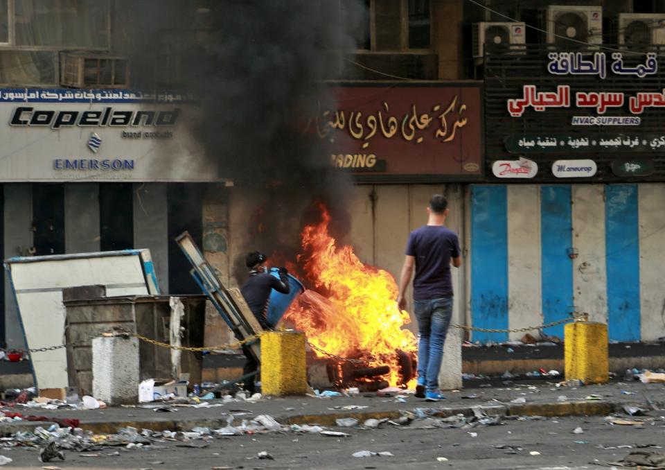 Protesters tries to extinguish a motorcycle burned by riot police during clashes between Iraqi security forces and anti-government protesters at Khilani Square in Baghdad, Iraq, Thursday, Nov. 14, 2019. (AP Photo/Hadi Mizban)