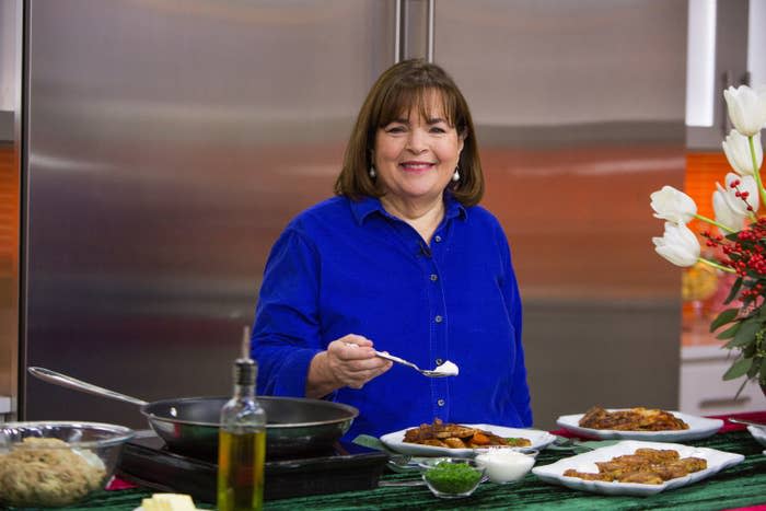 Garten stands in front of dishes and a pan while holding a spoon of white sauce