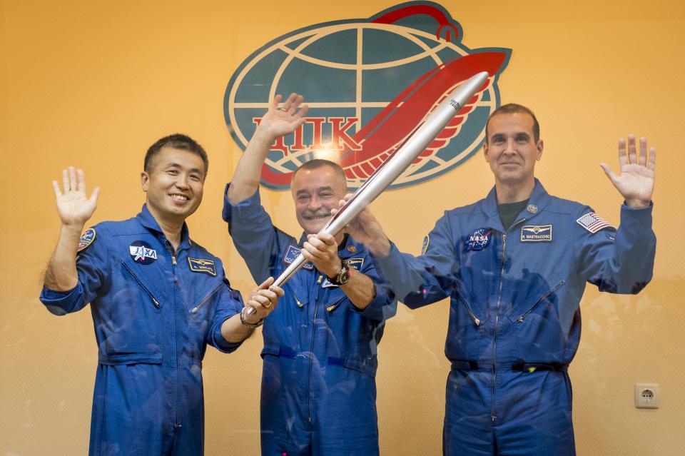 Expedition 38 Flight Engineer Koichi Wakata, Soyuz Commander Mikhail Tyurin and Flight Engineer Rick Mastracchio smile as they hold an Olympic torch that will be flown with them to the International Space Station