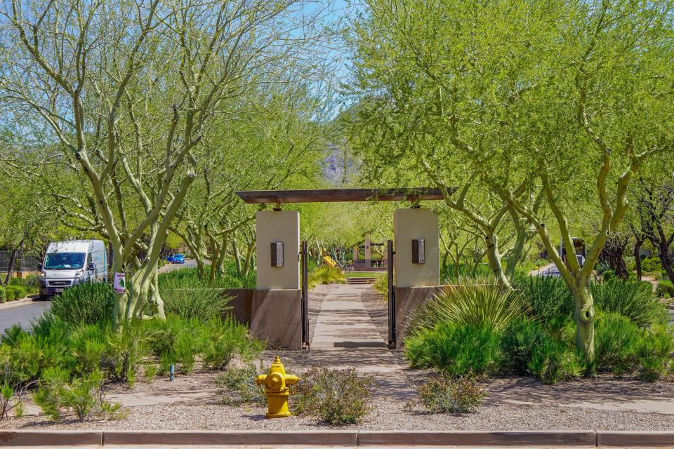 gates open up to a park with trees and bushes lining a bath leading to a playground with a yellow slide