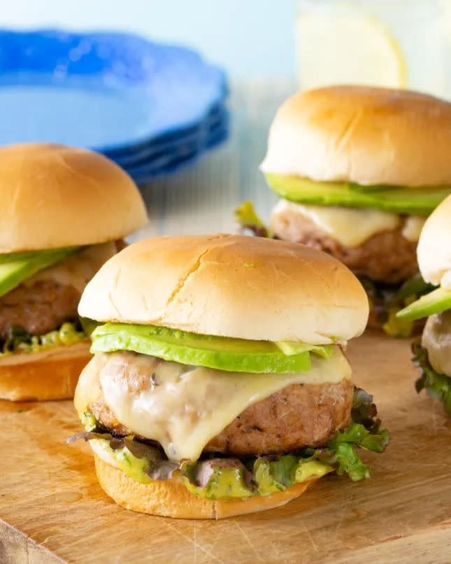 turkey burgers with avocado on buns on wood board