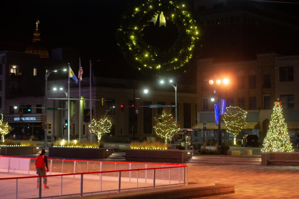 Lit wreaths and trees wrapped in lights are seen at Evergy Plaza while a lone skater takes to the ice at the CoreFirst Ice Rink Monday evening.