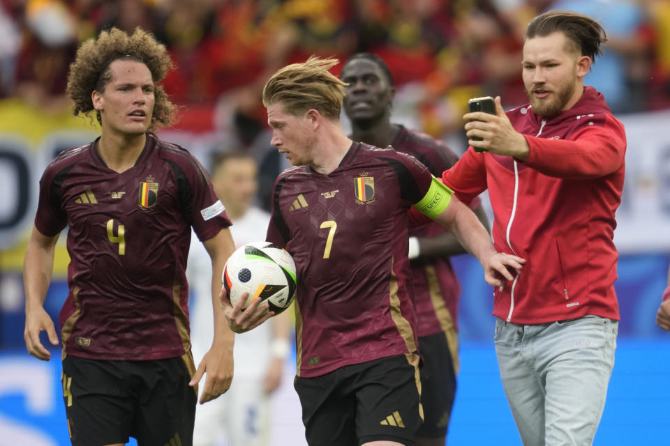 A pitch invader, right, tries to take a selfie with Belgium's Kevin De Bruyne during a Group E match between Belgium and Slovakia at the Euro 2024 soccer tournament in Frankfurt, Germany, Monday, June 17, 2024. (AP Photo/Michael Probst)