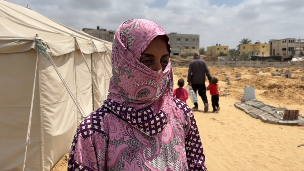 Rehab Abu Daqqa wearing a head scarf covering her mouth standing in front of a tent