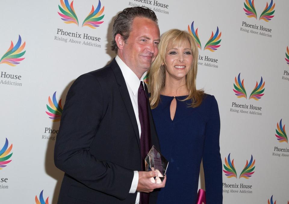 matthew perry and lisa kudrow stand together and smile for photos, he holds a crystal award