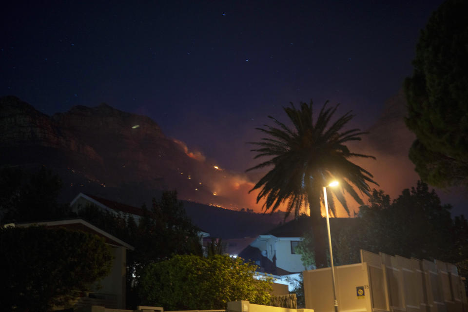 Residential neighborhoods are lit by raging fires in Cape Town, South Africa, Monday, April 19, 2021. Residents are being evacuated from Cape Town neighborhoods after a huge fire spreading on the slopes of the city's famed Table Mountain was fanned by strong winds overnight and threatened houses.(AP Photo/Jerome Delay)