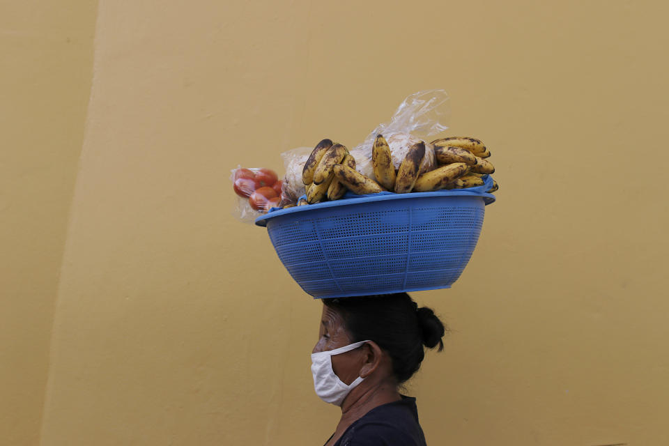 Guillerma Torres, wearing a face mask to curb the spread of the new coronavirus, carries a basket of fruit on her head to sell, on a street in Tegucigalpa, Honduras, Thursday, June 18, 2020. The hospitalization Wednesday of Honduras' president with COVID-19 and pneumonia has drawn attention to another country struggling under the pandemic's strain as cases rise exponentially in the capital. (AP Photo/Elmer Martinez)