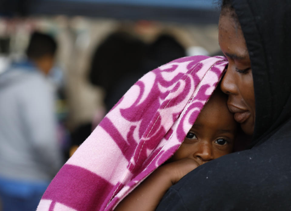 A Haitian migrant woman holds her baby as she waits in line to put her name on a migrant-run, months-long list to request U.S. asylum, alongside the El Chaparral pedestrian border crossing in Tijuana, Mexico, Friday, Nov. 30, 2018. Authorities in the Mexican city of Tijuana have begun moving some of more than 6,000 Central American migrants from an overcrowded shelter on the border to an events hall further away.(AP Photo/Rebecca Blackwell)