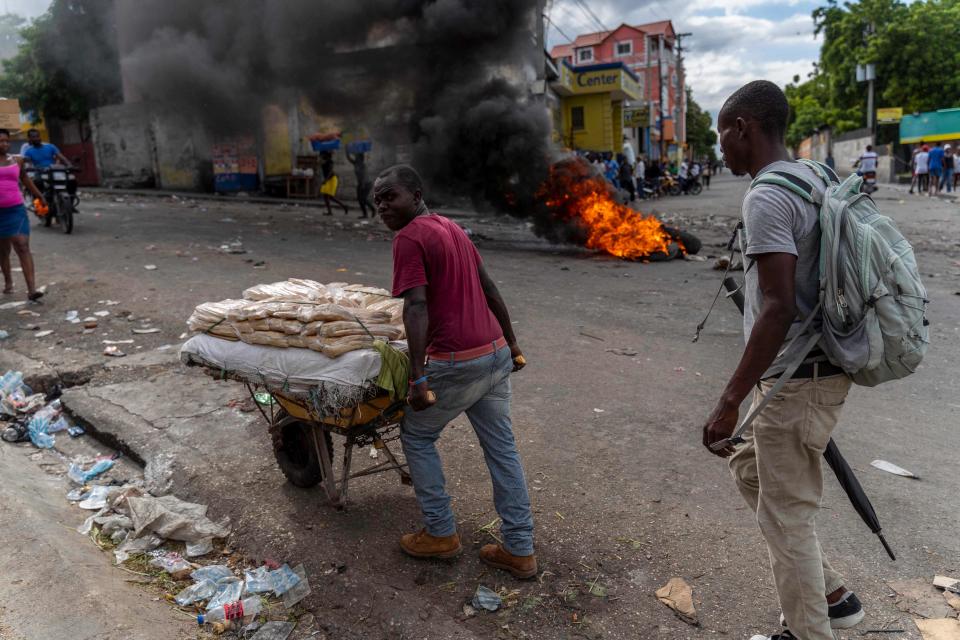 A bread vendor pushes his cart past a burning barricade during a protest against Haitian Prime Minister Ariel Henry calling for his resignation in Port-au-Prince, Haiti, Oct. 10, 2022. - Protests and looting have rocked the unstable country since Sept. 11, when Prime Minister Ariel Henry announced a fuel price hike.