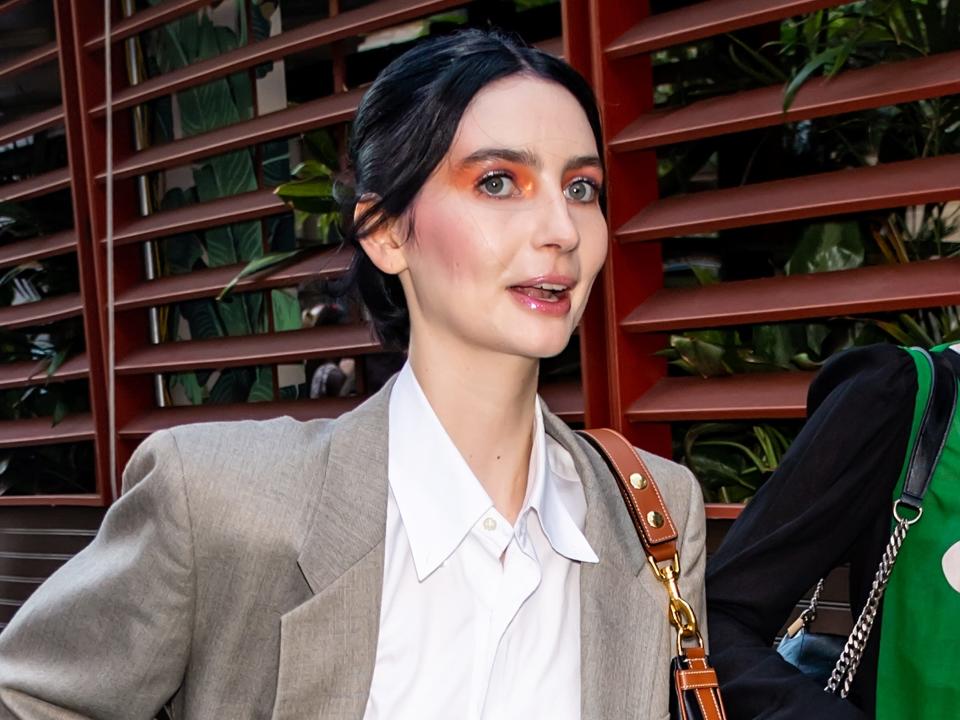 Meadow Walker (a tall, 22-year-old woman with dark black hair) walking while wearing blue jeans and a white collared shirt under a blazer.