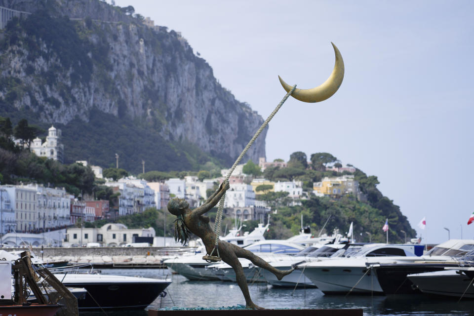 The bronze sculpture by Giacinto Bosco titled "swing on the moon" is backdropped by Capri's harbour, Wednesday, April 17, 2024. Group of Seven foreign ministers are meeting on the Italian resort island of Capri, with soaring tensions in the Mideast and Russia's continuing war in Ukraine topping the agenda. The meeting runs April 17-19. (AP Photo/Gregorio Borgia)