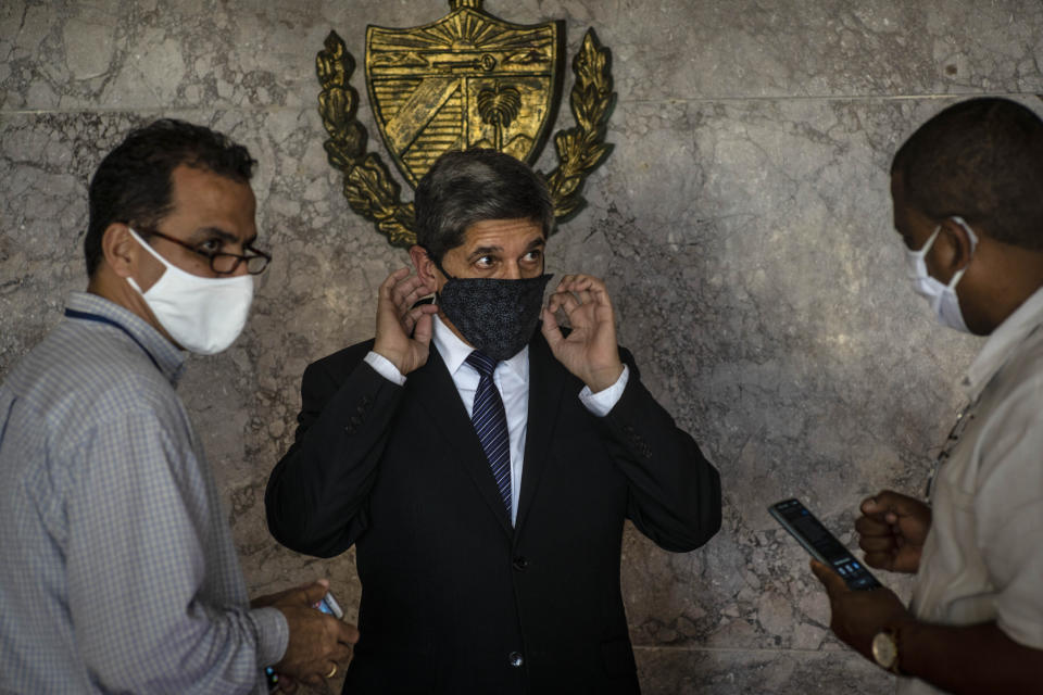 Cuba's Director General of U.S. Affairs Carlos Fernández de Cossio, center, puts on a mask as a precaution against the spread of the new coronavirus, after a press conference in Havana, Cuba, Tuesday, Jan. 12, 2021. The Trump administration has re-designated Cuba as a "state sponsor of terrorism "in a move that hits the country with new sanctions shortly before President-elect Joe Biden takes office. (AP Photo/Ramon Espinosa)