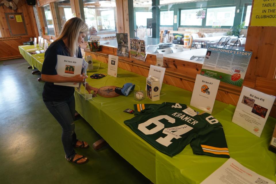 Lisa Schraufnagel of Nashotah arranges silent auction items at the 2023 Christopher's Shoot Against Childhood Cancer at the Waukesha Gun Club. The event is named for her late son. The sporting clays event and auctions raised $278,773 for the MACC Fund.