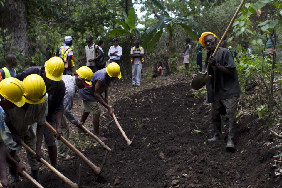 In this April 10, 2012 photo, Genove Valcimon 70, right, plays music using his shovel as laborers work to his rhythm as they build a road that will lead to an exploratory drill site in the department of Trou Du Nord, Haiti. Haiti's land may yet hold the solution to centuries of poverty: there is gold hidden in its hills, and silver and copper too. Now, two mining companies are drilling around the clock to determine how to get those metals out, and how much it might cost. (AP Photo/Dieu Nalio Chery)