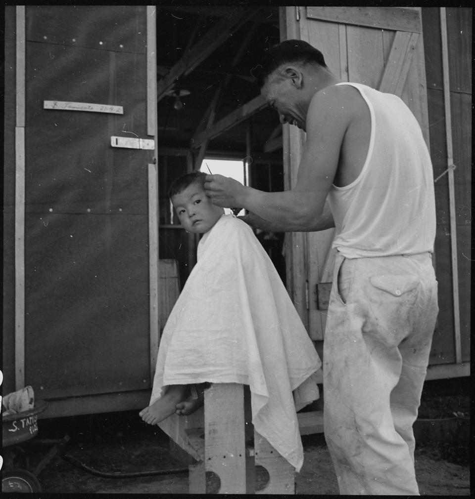 Manzanar Relocation Center, Manzanar, California. Little evacuee of Japanese ancestry gets a haircut