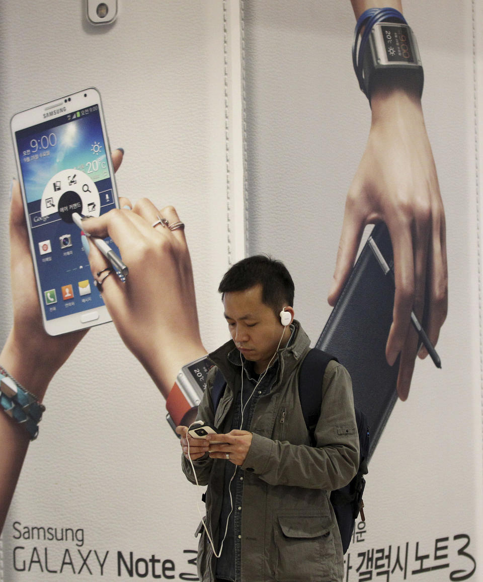 A man uses a smartphone near an advertisement for Samsung Electronics Co.'s Galaxy Note 3 in Seoul, South Korea, Tuesday, April 8, 2014. Declining smartphone prices hit profit at Samsung for a second straight quarter. The consumer technology heavyweight said Tuesday that it expects operating income of about 8.4 trillion won ($8 billion) for the January-March quarter, down 4 percent from a year earlier. (AP Photo/Ahn Young-joon)