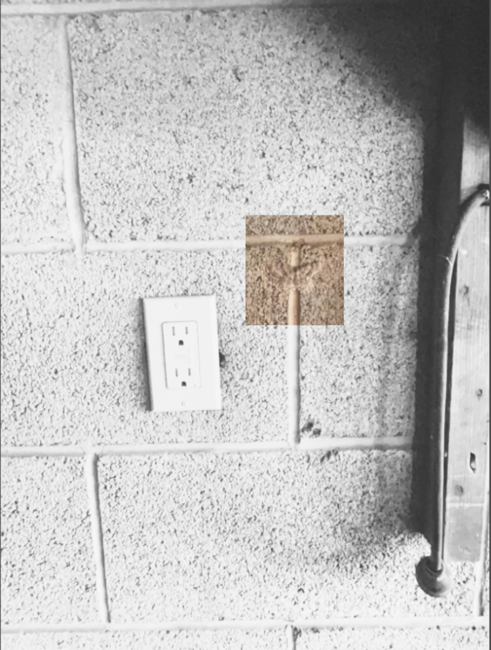 An electrical outlet is installed on a cinder block wall near a vertical metal beam
