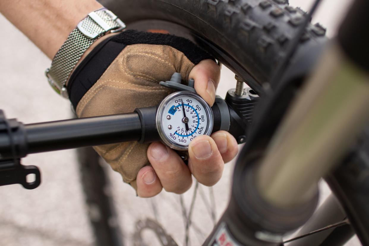 man checking tire pressure of e bike, inflating air with hand pump;