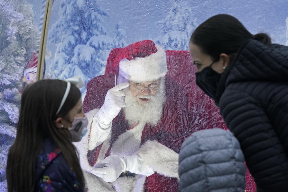 Santa, portrayed by Dan Kemmis, talks to a family wearing masks as he sits inside a protective bubble in Seattle's Greenwood neighborhood on Dec. 8, 2020. Kemmis has been Santa in past years, but he started his daily appearances early this year and added his "snow globe" tent due to the Coronavirus pandemic. In this socially distant holiday season, Santa Claus is still coming to towns (and shopping malls) across America but with a few 2020 rules in effect. (AP Photo/Ted S. Warren)