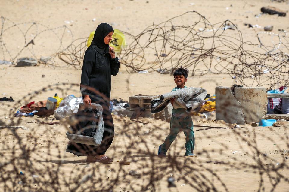 A woman and boy walk with belongings past barbed-wire fences as they flee from Rafah (AFP via Getty Images)