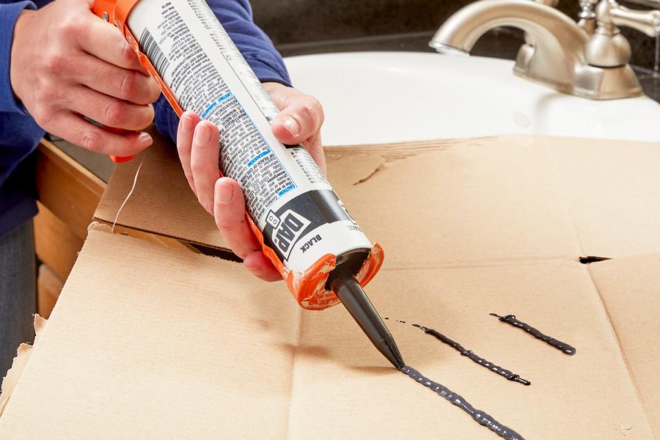 Woman tests a caulk gun on cardboard to make sure caulk is coming out.