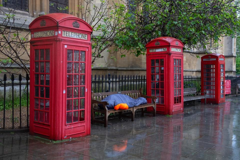 A homeless person sleeps in the rain between phone-boxes in central London (Getty Images)