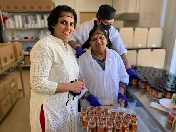 Shivani Dhamija, left, her mother Rani Dhamija, centre, and another worker at Shivani's Kitchen stand alongside jars of spice mix. (Shaina Luck/CBC - image credit)