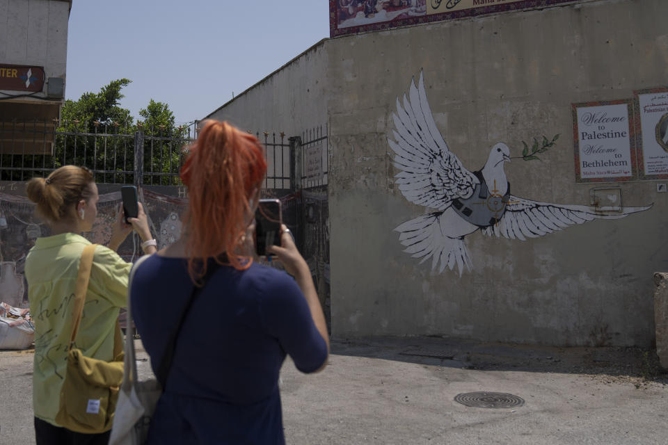 Turistas toman fotos de un mural del reservado artista de grafiti británico Banksy en la ciudad de Belén, Cisjordania, el jueves 4 de agosto de 2022. (Foto AP/Nasser Nasser)