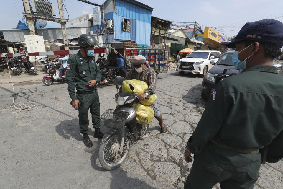 A vendor, center, carries dead chickens for a nearby market as local police officers stand guard at a blocked street near Phnom Penh International airport in Phnom Penh, Cambodia, Thursday, April 15, 2021. Cambodia’s leader said that the country’s capital Phnom Penh will be locked down for two weeks from Thursday following a sharp rise in COVID-19 cases. (AP Photo/Heng Sinith)